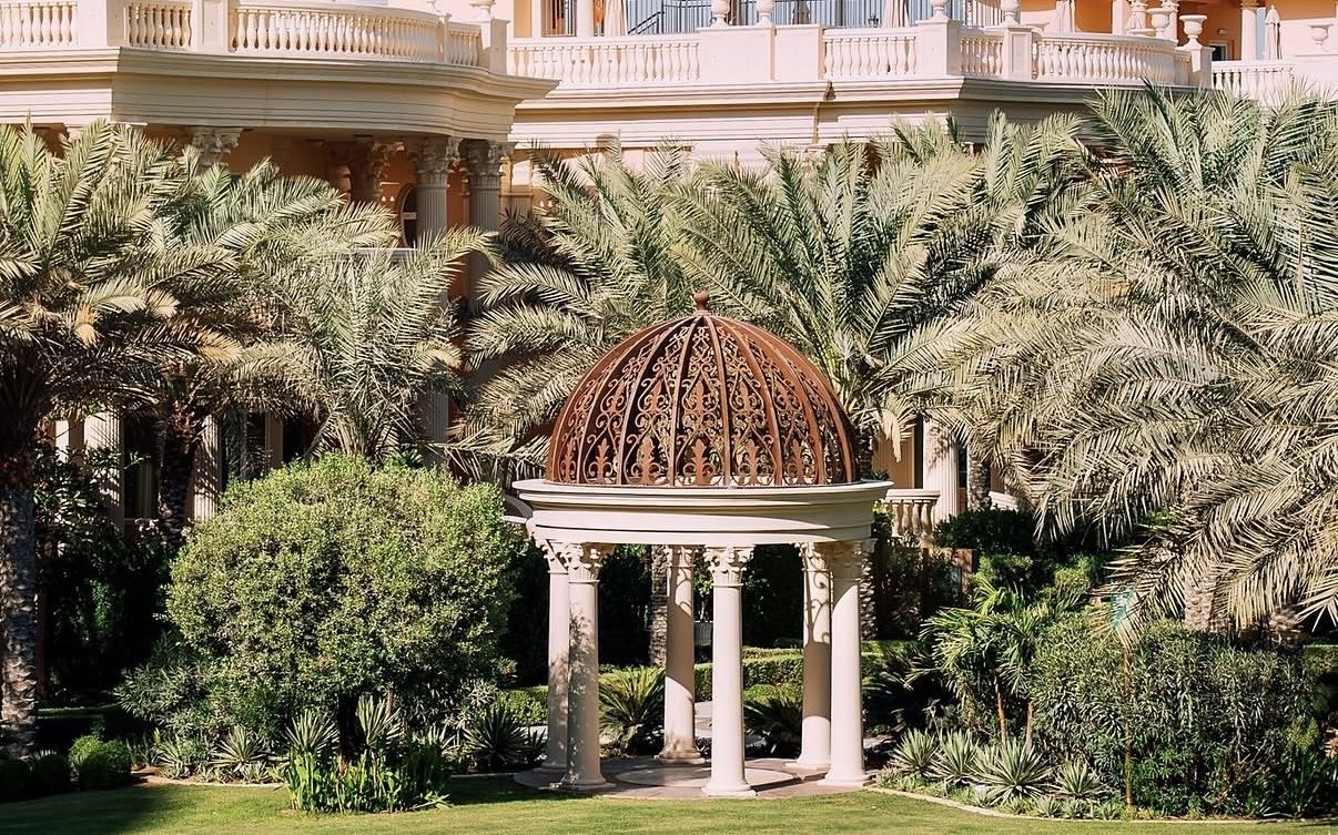 A white colonnaded gazebo with a copper filigree dome on a palace lawn among palms